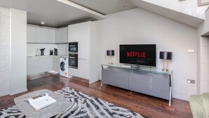 A modern living room with a flat-screen TV, a glass console table, a sofa, and a staircase. - Modern Times - Covent Garden By Frankie Says (London)