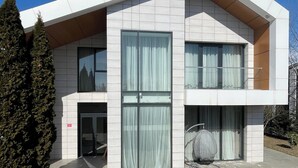 A modern two-story building with large windows, a covered outdoor seating area, and a paved entrance.