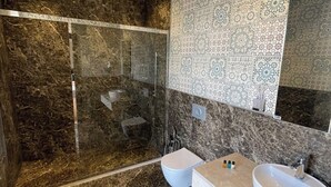 A modern bathroom with a walk-in shower, two sinks, and patterned tiles.