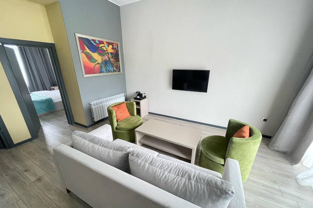 Una sala de estar moderna con un sofá, dos sillones, una mesa de centro, un televisor de pantalla plana montado en la pared y un radiador.