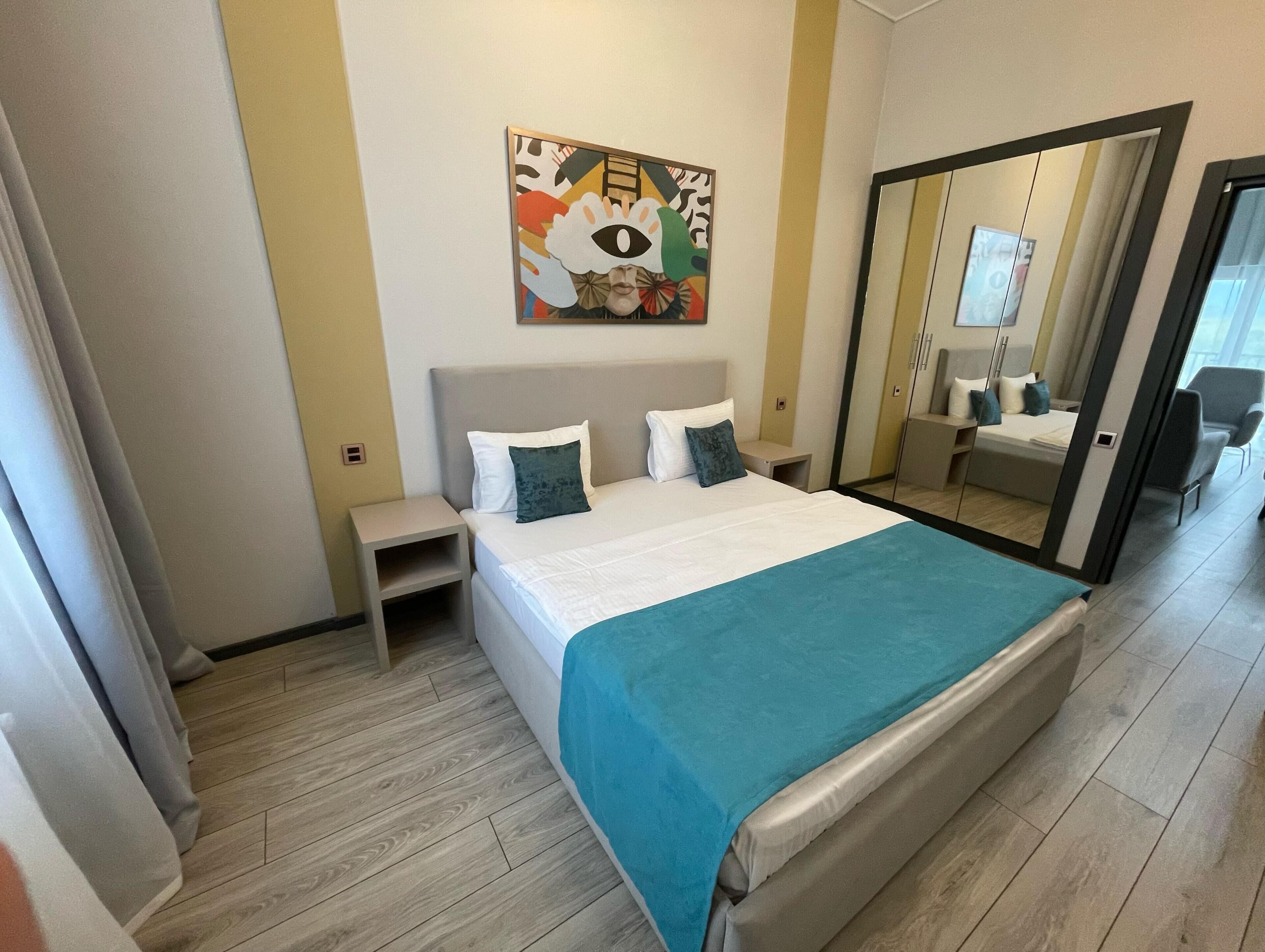 Un dormitorio moderno con una cama grande, una mesita de noche, un espejo y un cuadro abstracto colorido en la pared.