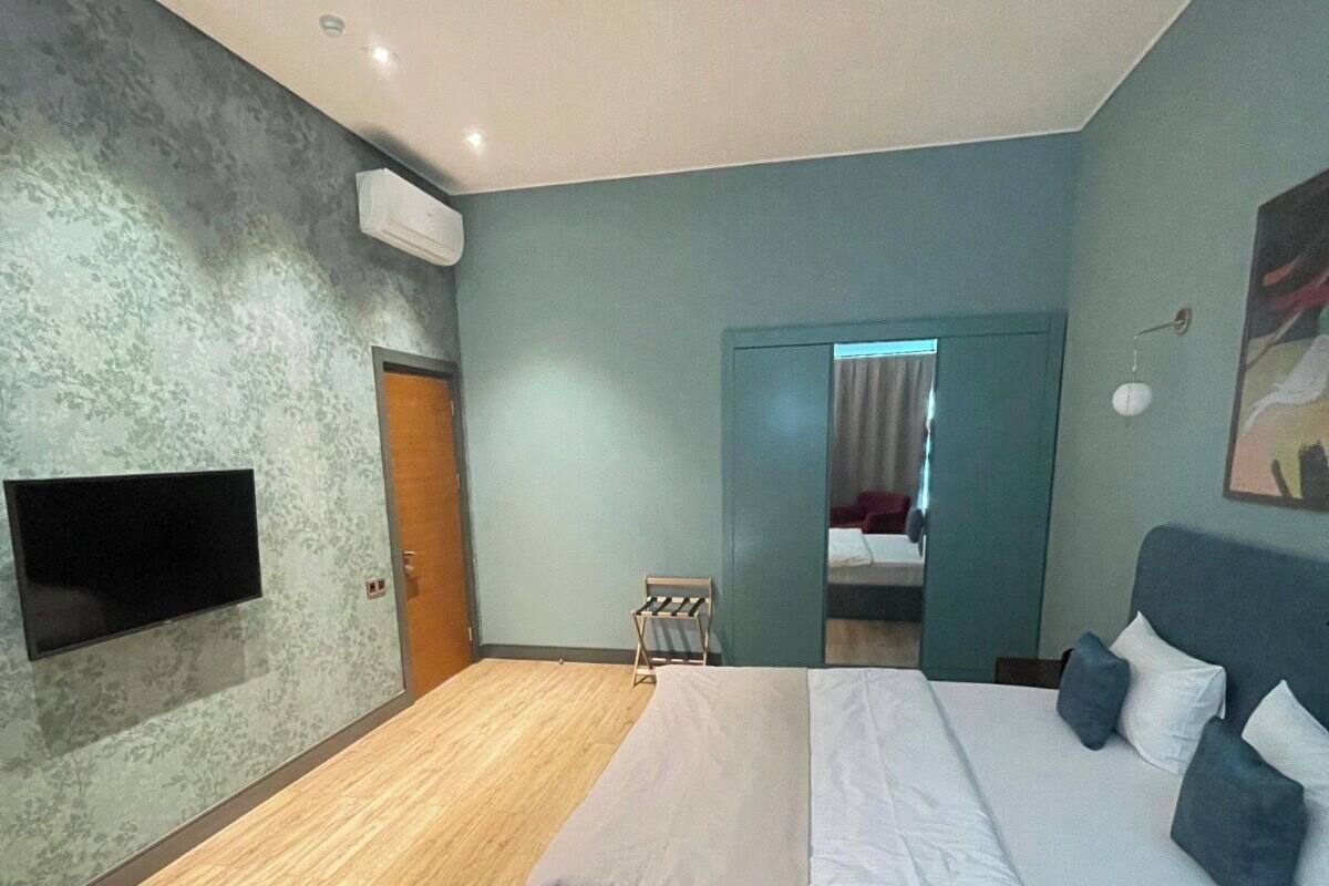 Un dormitorio moderno con una cama grande, un televisor de pantalla plana montado en la pared y piso de madera.