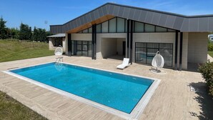 Een modern huis met een zwembad, grote ramen en buitenmeubilair.