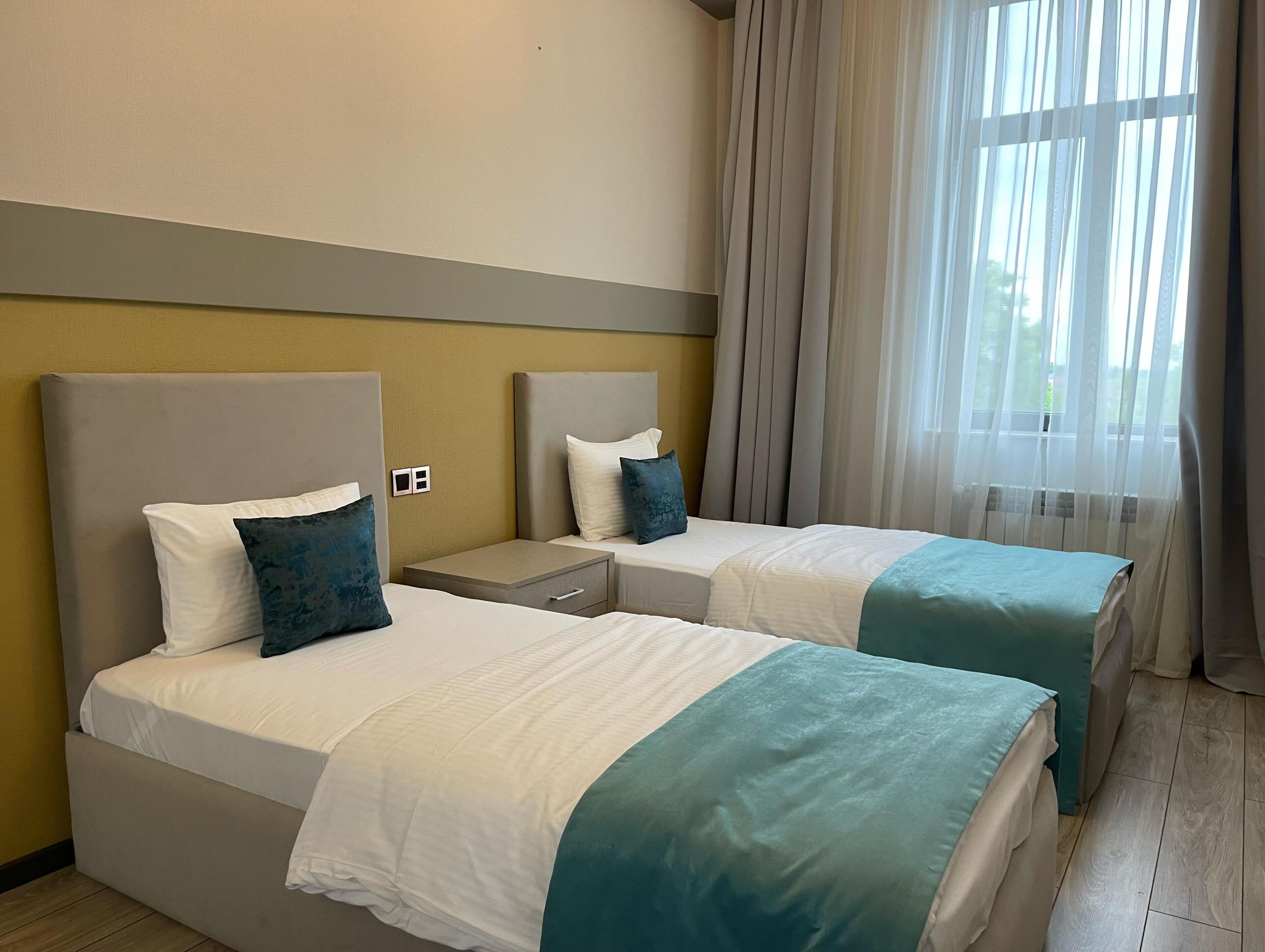A hotel room with two beds, a nightstand, and a window with curtains.
