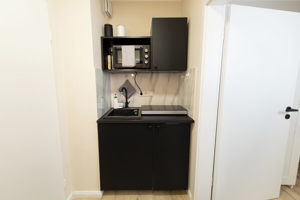 A compact kitchenette with a microwave, a small sink, and a cabinet.