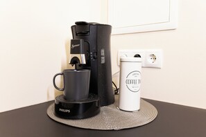 A coffee maker, a mug, and a coffee tin on a table.
