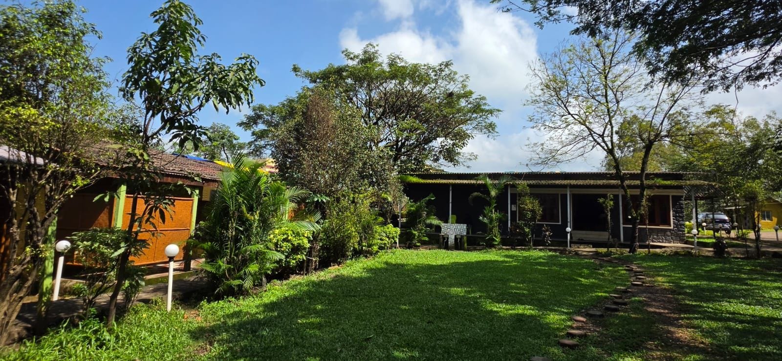 A residential property with a covered outdoor seating area, a well-maintained lawn, and a variety of trees and shrubs.
