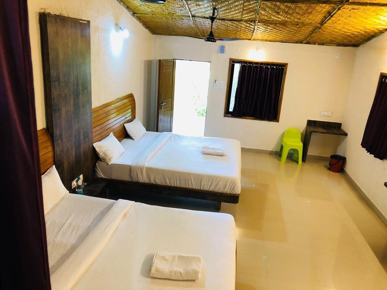 A room with two beds, a small table, a chair, and a window with curtains.