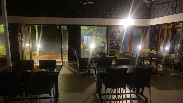 Uma área de refeições interna com mesas e cadeiras, janelas amplas e uma parede de pedra.