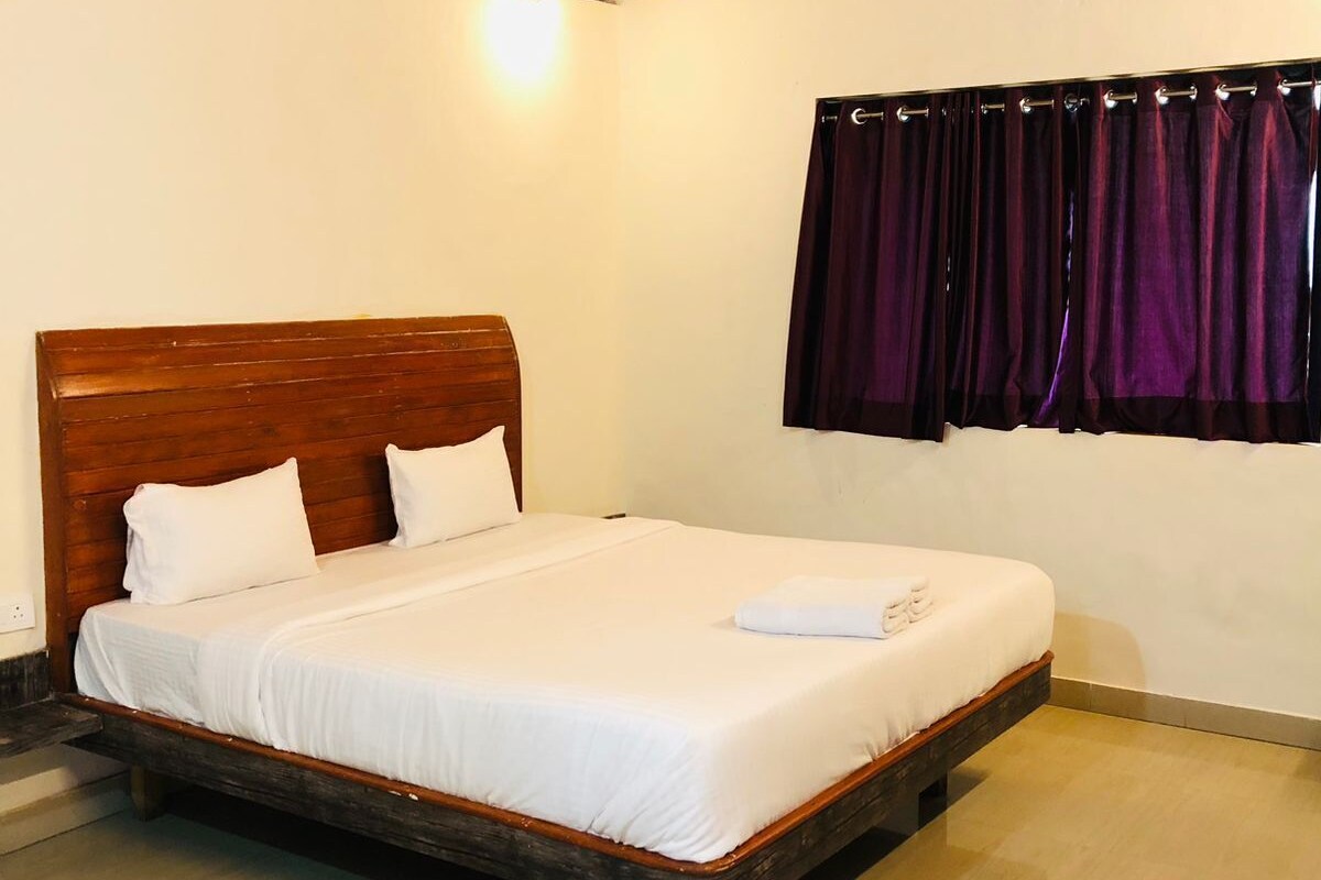 A single bed with a wooden headboard in a room with a wooden ceiling and a window with purple curtains.