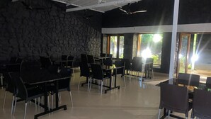 Amplo espaço interno com várias mesas e cadeiras, paredes de pedra e grandes janelas que proporcionam iluminação natural.