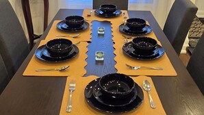 Mesa de comedor lista para seis personas, con platos negros, cubiertos y una jarra sobre una mesita auxiliar.