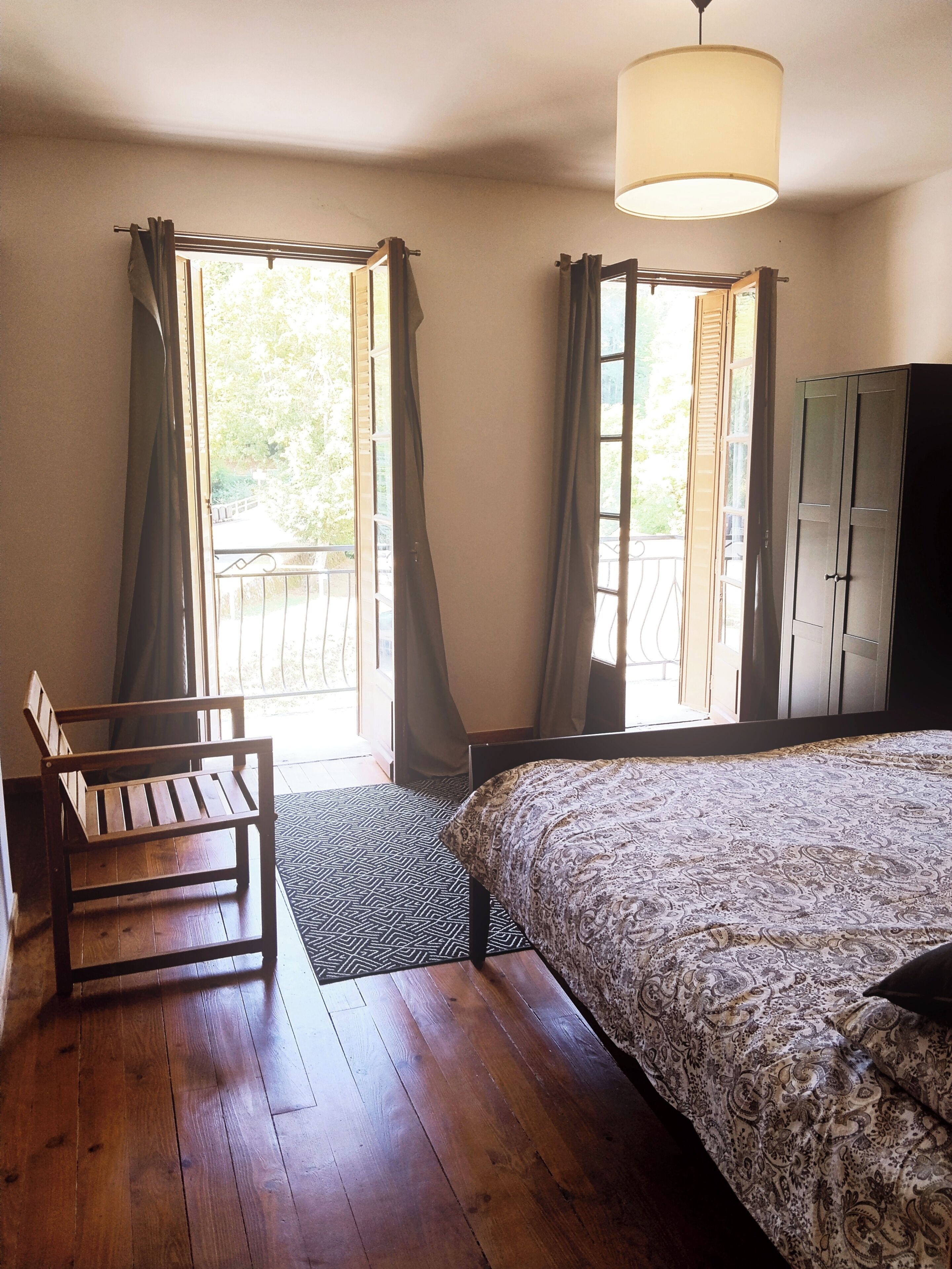 Une pièce comprenant un lit, une chaise, une armoire et deux fenêtres avec des rideaux.