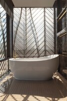 Un baño moderno con una bañera independiente, un ventanal con diseño geométrico y una encimera de mármol.