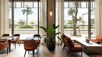Un moderno vestíbulo de hotel con ventanas amplias, una planta central y zonas de estar.
