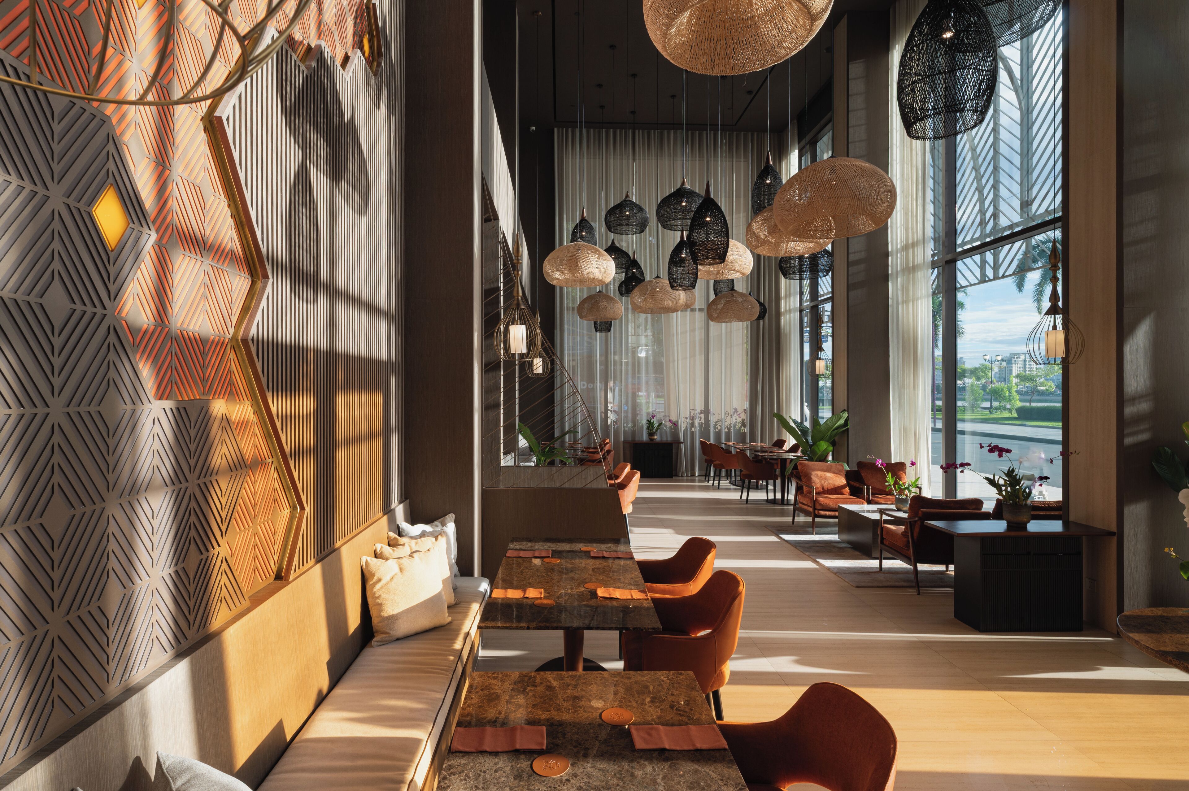A modern dining area with a long table, orange chairs, and hanging pendant lights.