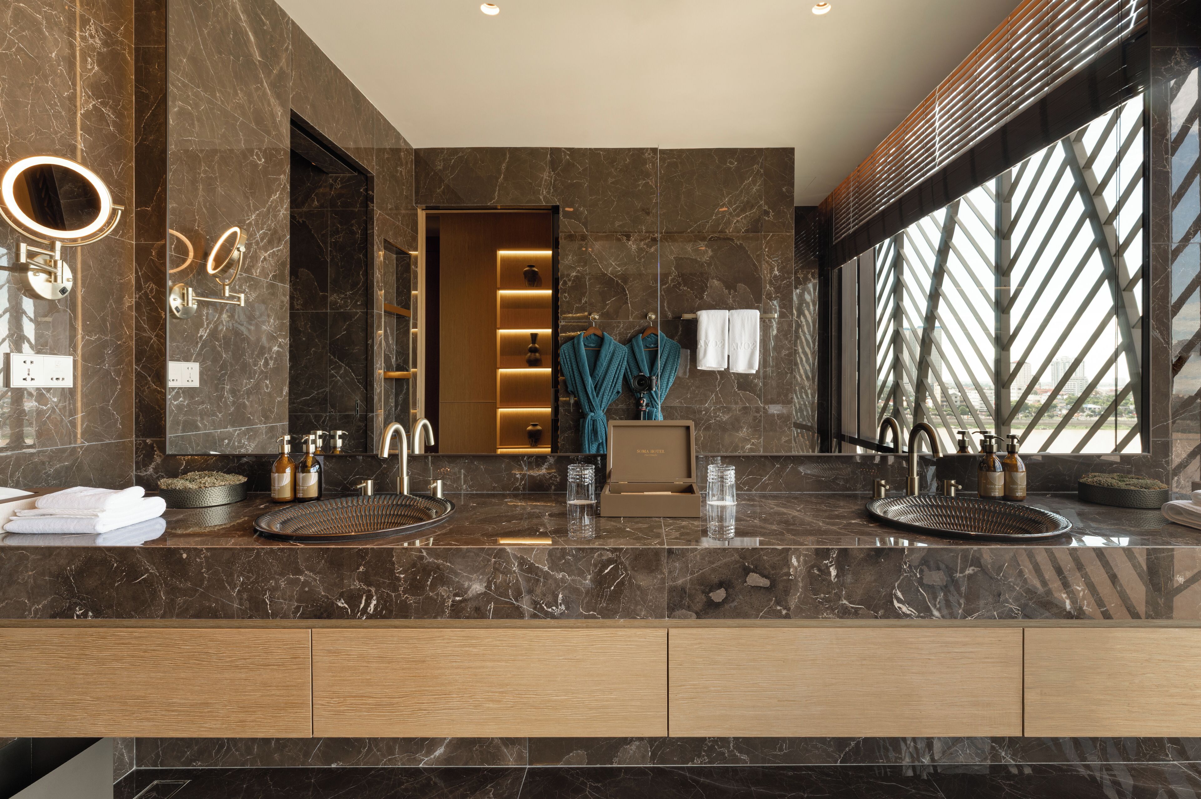 Un baño moderno con dos lavamanos, paredes de mármol y un ventanal grande.