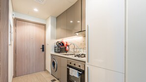 A compact kitchen with a washing machine, oven, microwave, and a sink with a hose. - Studio Near Meydan Racecourse, Minutes to Downtown, Azizi Riviera 47 by Deluxe Holiday Homes (Dubai)