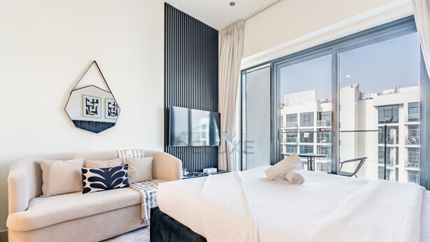 A modern hotel room with a large bed, a sofa, a TV, and a view of the cityscape. - Studio Near Meydan Racecourse, Minutes to Downtown, Azizi Riviera 47 by Deluxe Holiday Homes (Dubai)