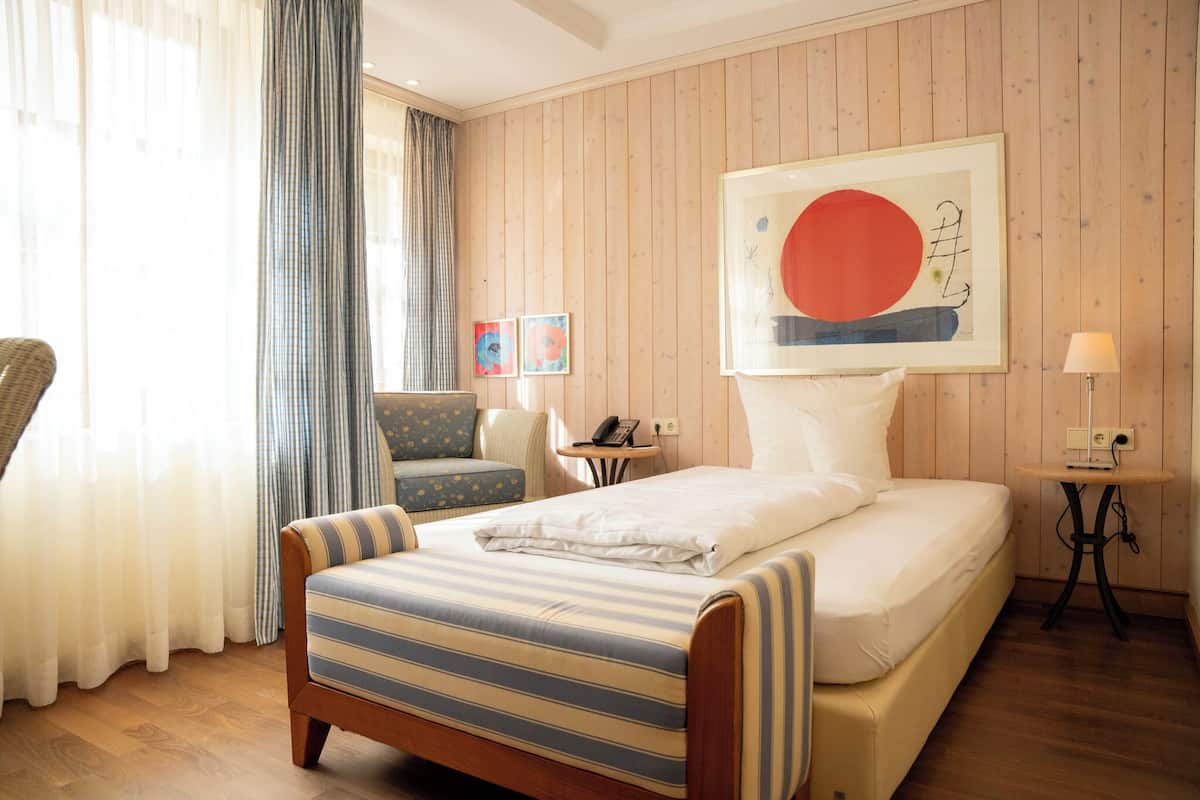 A hotel room with a bed, a chair, a small table, and a wall with artwork.