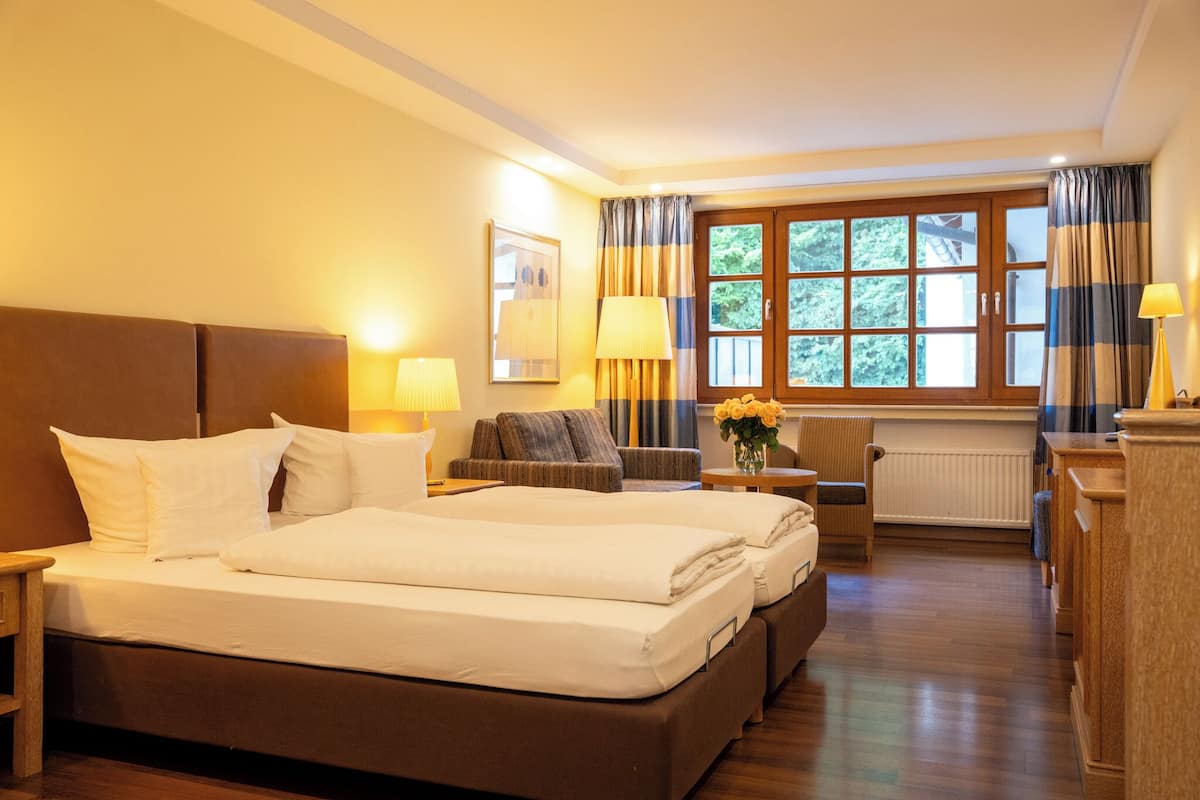 A hotel room with a large bed, a sofa, a chair, a table, and a window with curtains.
