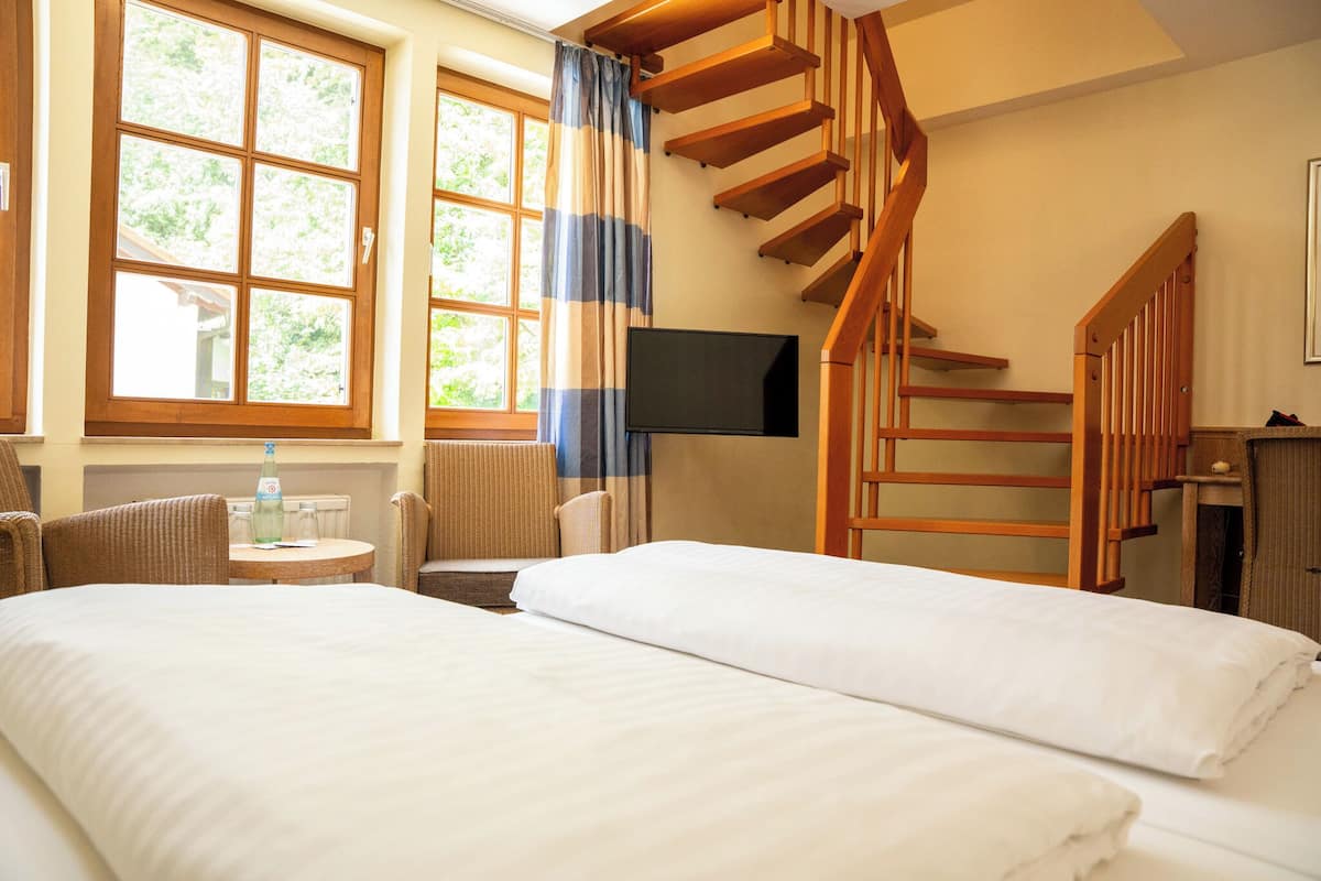 A hotel room with two beds, a TV, a wooden staircase, and a window with curtains.