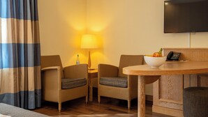 Camera d'albergo con un tavolo da pranzo in legno, due poltrone imbottite, una lampada, una TV a muro e un letto con tenda a righe.
