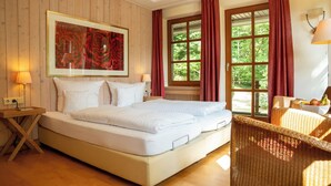 Una camera da letto con un grande letto, pareti in legno, una finestra con tende, un comodino con una lampada e una sedia in vimini.
