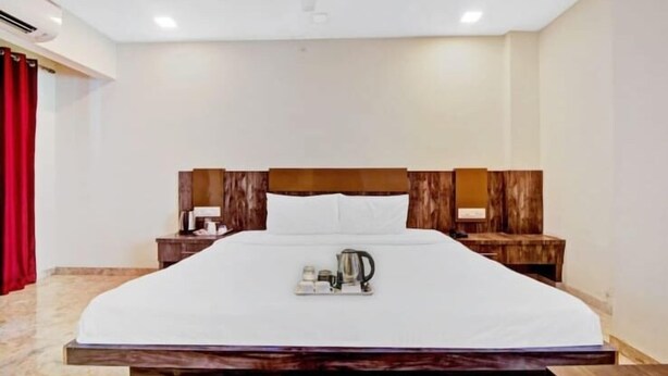 A hotel room with a large bed, wooden headboard, two bedside tables with lamps, and a tray with a kettle and cups on the bed. - Hotel Krishna  (Nagpur)