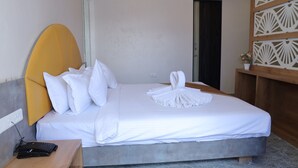 A neatly made bed with white linens, a wooden headboard, and a small bedside table with a remote control. - Hotel Krishna  (Nagpur)