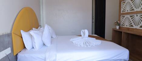 A neatly made bed with white linens, a wooden headboard, and a small bedside table with a remote control.
