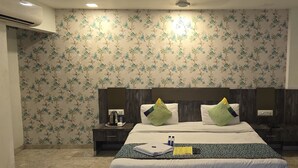 A hotel room with a floral wallpaper, a bed with two pillows, a bedside table with a kettle, and a nightstand with a phone. - Hotel Krishna  (Nagpur)