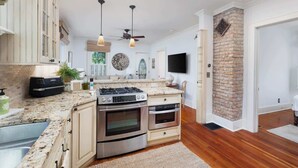 A modern kitchen with granite countertops, stainless steel appliances, and a brick accent wall. - Charming 3BR Cottage + Garden, Walk to Downtown & Metra, Sleeps 6 (Geneva)