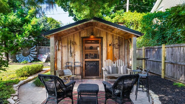 A wooden cabin with a porch, two chairs, a table, and a bench. - Charming 3BR Cottage + Garden, Walk to Downtown & Metra, Sleeps 6 (Geneva)