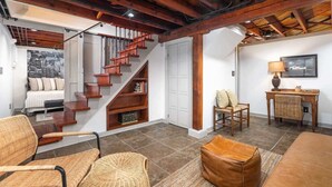 A spacious living area with a wooden staircase, a comfortable sofa, wicker chairs, and a desk with a lamp. - Charming 3BR Cottage + Garden, Walk to Downtown & Metra, Sleeps 6 (Geneva)
