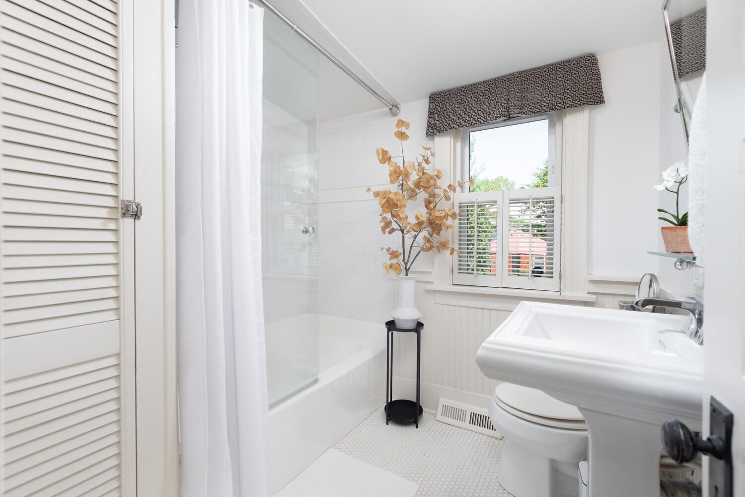 A modern bathroom with a glass shower, white tiles, a toilet, and a sink.