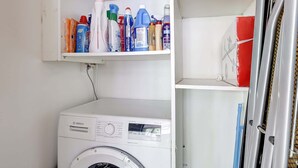 A white Bosch washing machine with a control panel, a shelf above it with various cleaning products, and a red box on the right. - Appartement chic avec terrasse -  Champs-Elysées (Paris)