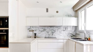 Een moderne keuken met witte kasten, een marmeren spatwand en een inbouwoven.