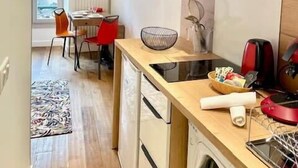 A modern kitchen with a built-in washing machine, a dining area with a red chair, and a large window. - Ben Nevis charming studio in the heart of the lively life of the Pré Carré (Annecy)