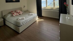 A bedroom with a bed, a nightstand, a dresser, a window with curtains, a radiator, and a painting on the wall. - TOBIA HOUSE Beautiful Lake View (San Rocco)