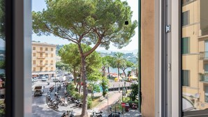 A view from a window overlooking a street with parked scooters, a large tree, and buildings in the background. - Charming Apartment Santa Margherita Ligur (Santa Margherita Ligure)
