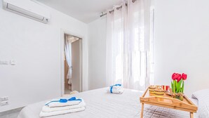 Une chambre d’hôtel avec un lit, un plateau en bois contenant des serviettes et un vase de tulipes rouges, et une salle de bain visible à travers une porte ouverte.