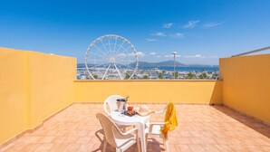 Un balcon donnant sur une grande roue, une table avec des chaises et une veste jaune posée sur une chaise.