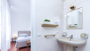Une chambre d’hôtel comprenant un lit, une table de chevet et une salle de bain avec un lavabo, un miroir et un porte-serviettes.
