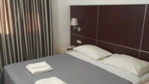 A hotel room with a bed, two pillows, a nightstand, a lamp, and a striped curtain. - Jolly house 1 (Cosenza)