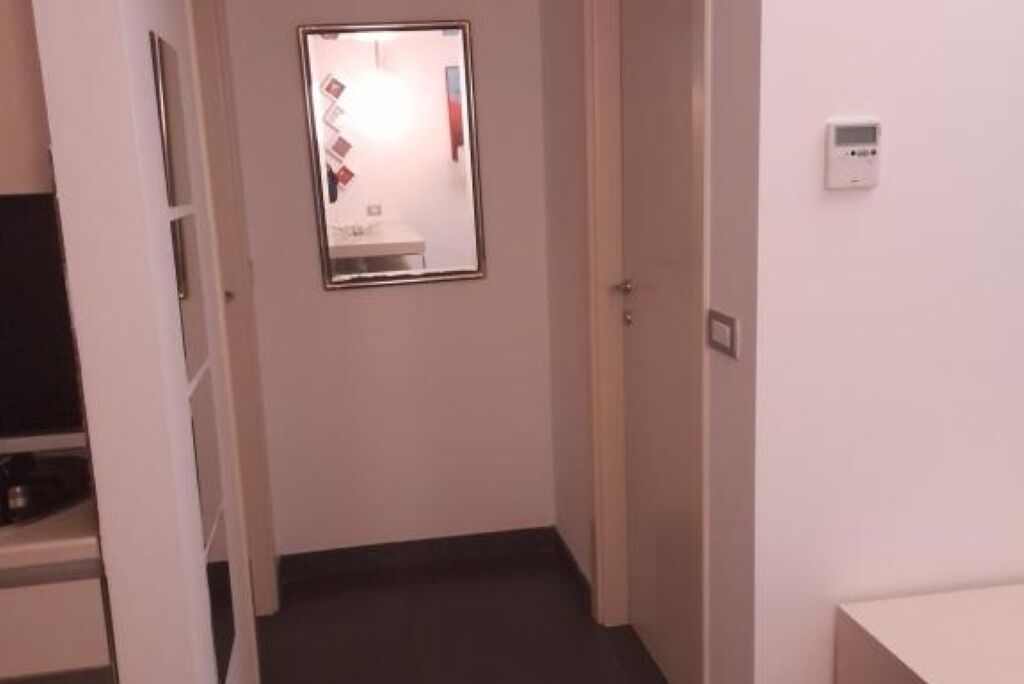 A narrow hallway with a door leading to a bathroom, a small window, and a thermostat on the wall.