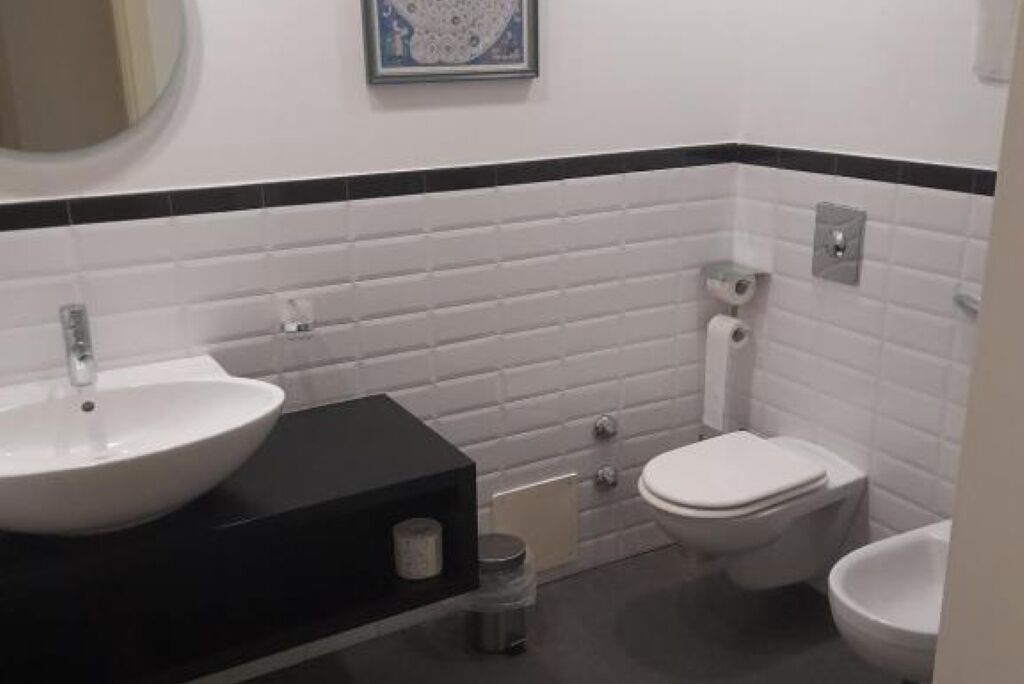 A bathroom with a white sink, black countertop, white toilet, and a bidet.