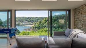 Una sala de estar moderna con un sofá y una mesa de fútbol, con amplias ventanas que ofrecen vistas a un paisaje costero.