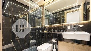 Un bagno moderno con un WC bianco, un lavandino e uno specchio. Le pareti presentano un motivo in marmo nero con venature dorate.