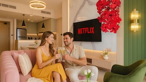 A modern living room with a pink sofa, a green armchair, and a flat-screen TV displaying 'NETFLIX'. - KeyRock Living - Golf Gate Apartment  (Dubai)